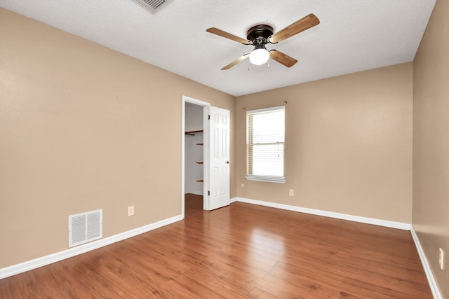 unfurnished bedroom with a closet, a spacious closet, wood-type flooring, a textured ceiling, and ceiling fan