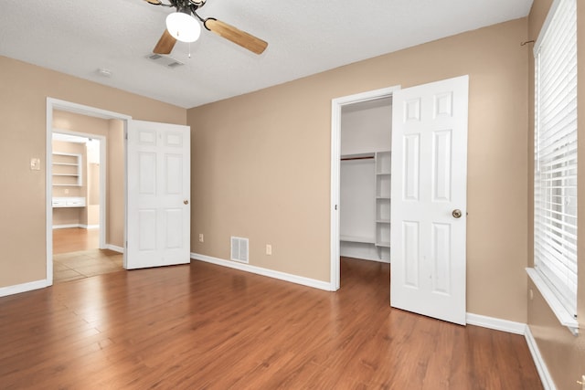 unfurnished bedroom with hardwood / wood-style floors, a textured ceiling, ceiling fan, a closet, and a spacious closet