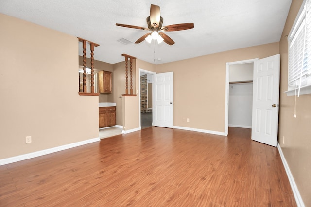 unfurnished bedroom featuring wood-type flooring, a textured ceiling, ceiling fan, a closet, and a walk in closet