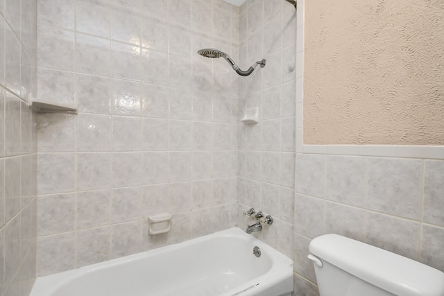 bathroom with tiled shower / bath, toilet, and tile walls