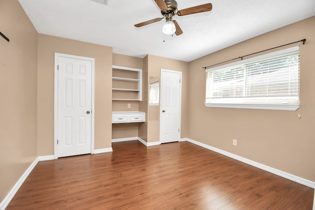 unfurnished bedroom featuring built in desk, ceiling fan, dark hardwood / wood-style floors, and a textured ceiling