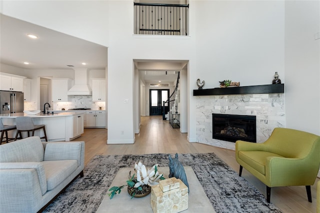 living room featuring a fireplace, light hardwood / wood-style floors, a towering ceiling, and sink