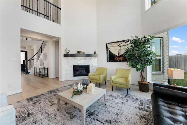 living room featuring a towering ceiling, light wood-type flooring, and a stone fireplace