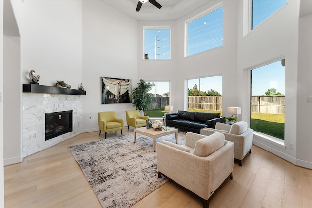 living room featuring light wood-type flooring, a towering ceiling, ceiling fan, and a fireplace