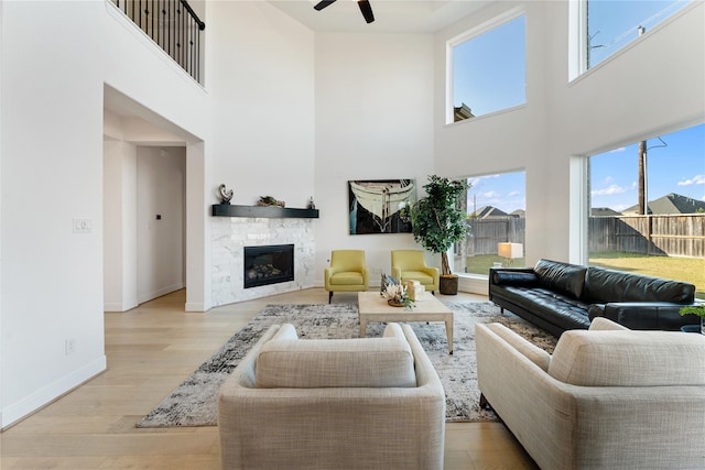 living room featuring a stone fireplace, plenty of natural light, light hardwood / wood-style floors, and a high ceiling