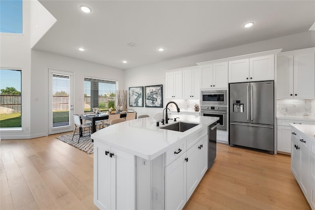 kitchen with white cabinetry, appliances with stainless steel finishes, light wood-type flooring, sink, and an island with sink