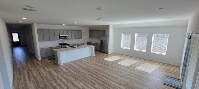 kitchen with a wealth of natural light, light hardwood / wood-style floors, an island with sink, and appliances with stainless steel finishes