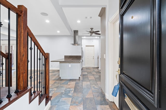 interior space featuring dark stone counters, wall chimney range hood, and ceiling fan