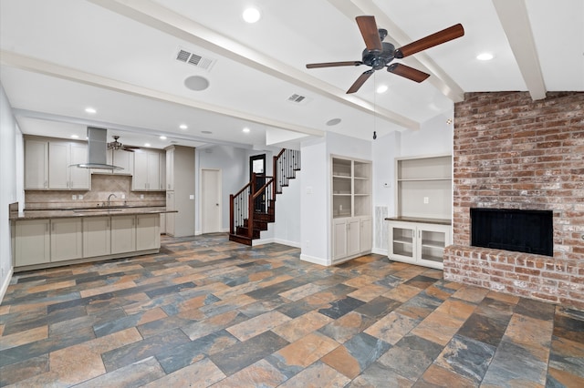 unfurnished living room featuring lofted ceiling with beams, sink, and a brick fireplace