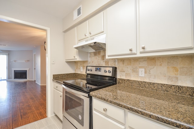 kitchen with backsplash, dark stone countertops, light wood-type flooring, stainless steel electric range oven, and white cabinetry