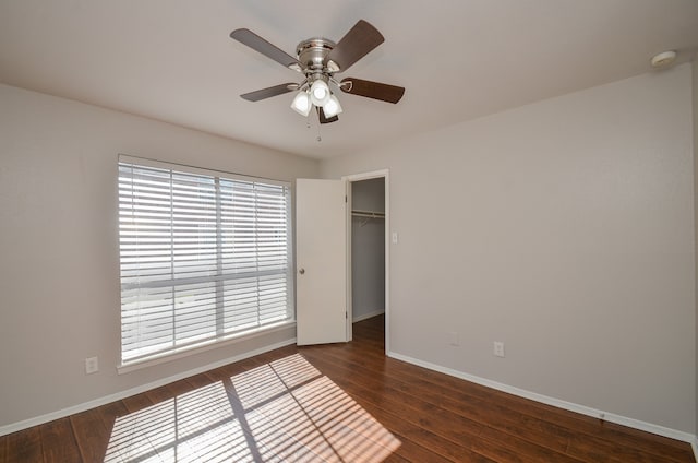 unfurnished bedroom featuring a closet, ceiling fan, dark hardwood / wood-style flooring, and a spacious closet