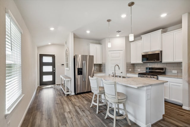 kitchen with a center island with sink, white cabinetry, appliances with stainless steel finishes, hanging light fixtures, and hardwood / wood-style floors