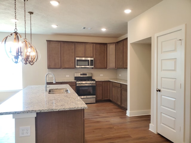 kitchen with visible vents, a sink, light stone counters, wood finished floors, and stainless steel appliances