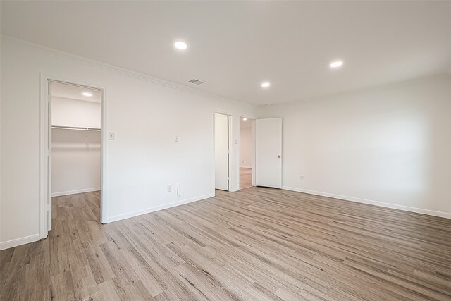 unfurnished bedroom with ornamental molding, light wood-type flooring, a walk in closet, and a closet