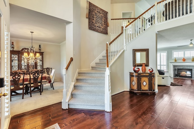 staircase with ornamental molding, hardwood / wood-style floors, ceiling fan with notable chandelier, and a towering ceiling