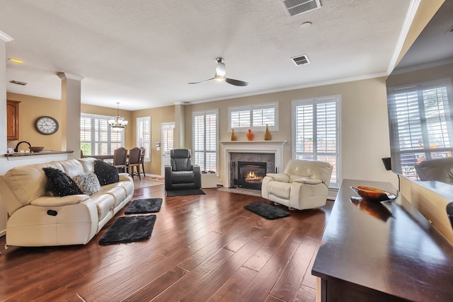 living room featuring crown molding, a textured ceiling, dark hardwood / wood-style flooring, a tiled fireplace, and ceiling fan with notable chandelier