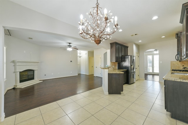 kitchen featuring light hardwood / wood-style floors, ceiling fan with notable chandelier, light stone counters, and tasteful backsplash