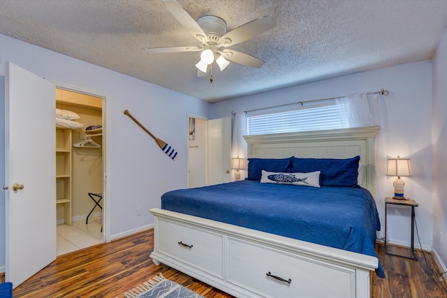 bedroom featuring a textured ceiling, hardwood / wood-style flooring, ceiling fan, a closet, and a spacious closet