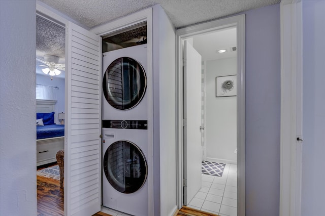 laundry room featuring stacked washer and dryer, ceiling fan, a textured ceiling, and light tile patterned floors