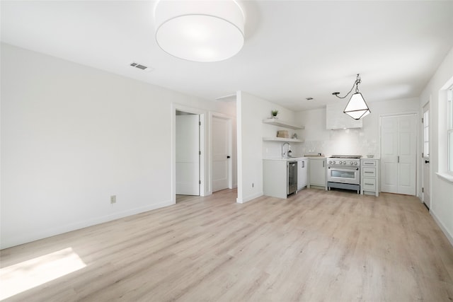 kitchen with tasteful backsplash, stainless steel appliances, sink, pendant lighting, and light hardwood / wood-style flooring