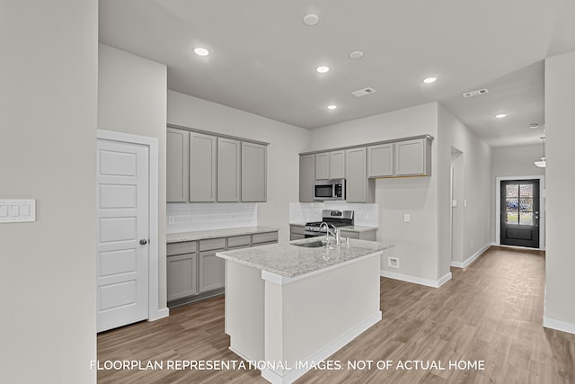 kitchen with a center island with sink, stainless steel appliances, light stone countertops, sink, and light hardwood / wood-style flooring