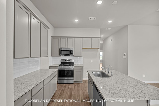 kitchen featuring stainless steel appliances, dark hardwood / wood-style flooring, a center island with sink, light stone counters, and sink