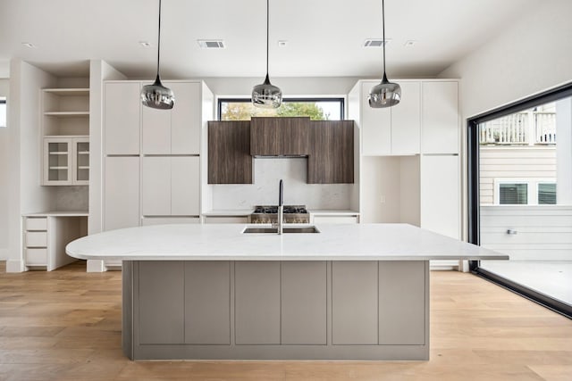 kitchen with light stone countertops, a kitchen island with sink, sink, pendant lighting, and light hardwood / wood-style flooring