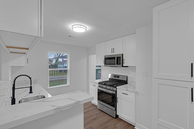 kitchen featuring sink, light stone counters, appliances with stainless steel finishes, light hardwood / wood-style flooring, and white cabinets