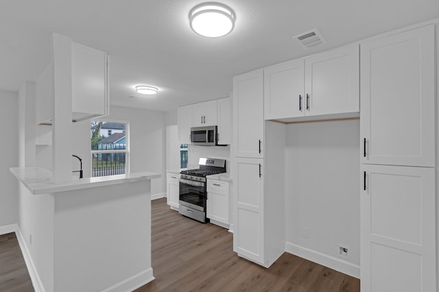 kitchen featuring white cabinets, kitchen peninsula, appliances with stainless steel finishes, and wood-type flooring