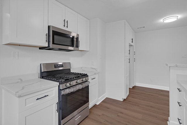 kitchen featuring stainless steel appliances, wood-type flooring, white cabinetry, and light stone counters