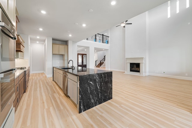 kitchen with dark stone counters, a spacious island, sink, ceiling fan, and light wood-type flooring