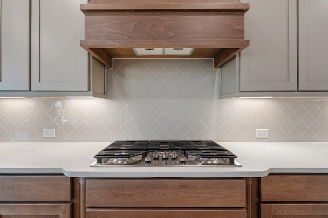 kitchen with decorative backsplash, light stone countertops, custom range hood, and stainless steel gas cooktop