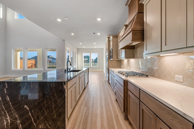 kitchen featuring sink, light hardwood / wood-style flooring, light stone countertops, custom range hood, and stainless steel gas cooktop