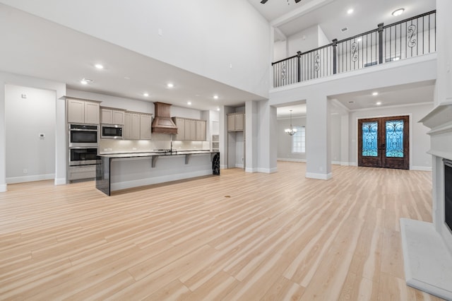 kitchen with custom exhaust hood, a center island with sink, light wood-type flooring, a kitchen bar, and stainless steel appliances