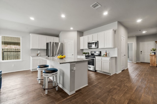 kitchen with stainless steel appliances, a kitchen island with sink, dark hardwood / wood-style floors, light stone countertops, and white cabinetry