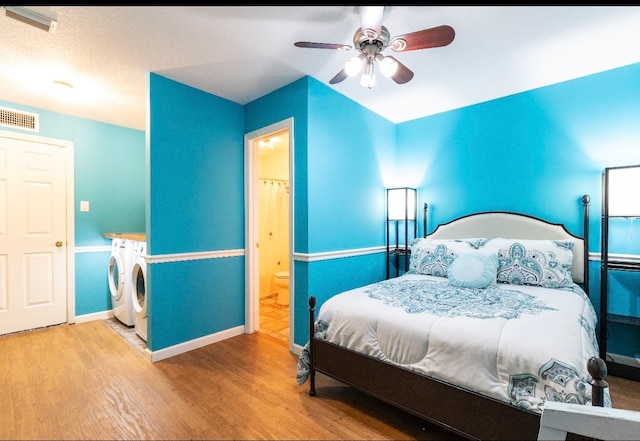 bedroom featuring light hardwood / wood-style floors, ceiling fan, washer and clothes dryer, and ensuite bathroom