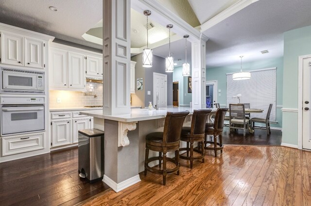 kitchen with white cabinetry, a center island with sink, dark hardwood / wood-style floors, hanging light fixtures, and white appliances