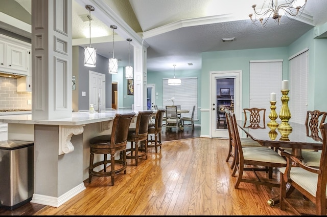 kitchen with tasteful backsplash, a textured ceiling, pendant lighting, a breakfast bar, and light hardwood / wood-style flooring