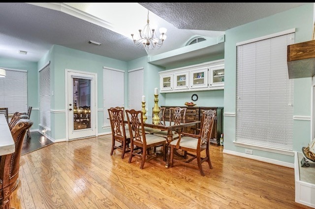 dining area featuring light hardwood / wood-style floors, a textured ceiling, and an inviting chandelier