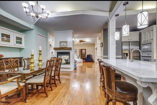 dining area with sink, ceiling fan with notable chandelier, a textured ceiling, a multi sided fireplace, and light wood-type flooring