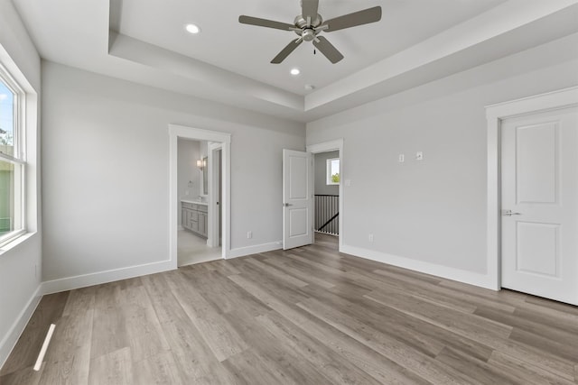 unfurnished bedroom featuring ceiling fan, light wood-type flooring, connected bathroom, and multiple windows