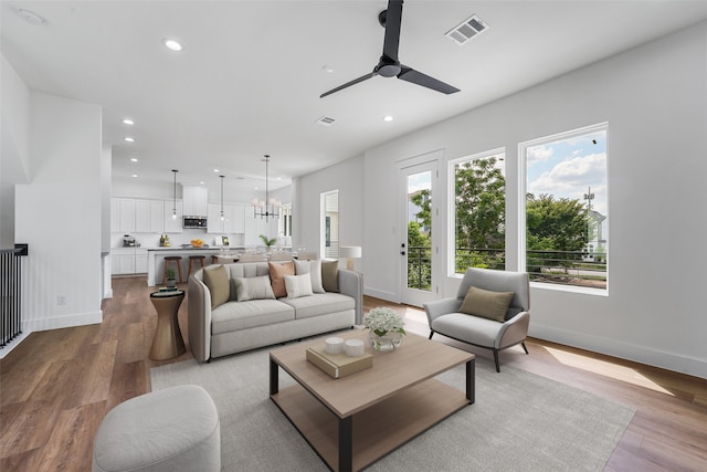 living room with ceiling fan with notable chandelier, light hardwood / wood-style flooring, and a healthy amount of sunlight