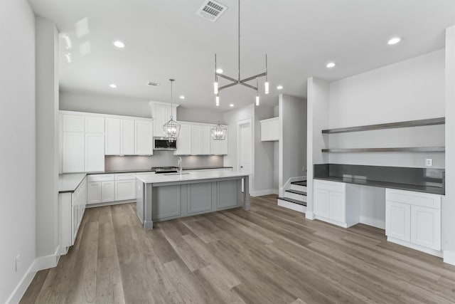 kitchen featuring hanging light fixtures, light wood-type flooring, white cabinetry, and a kitchen island with sink