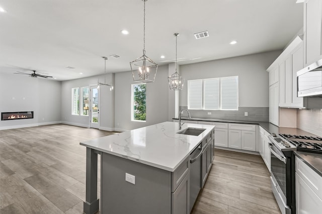 kitchen with sink, an island with sink, decorative light fixtures, white cabinets, and appliances with stainless steel finishes