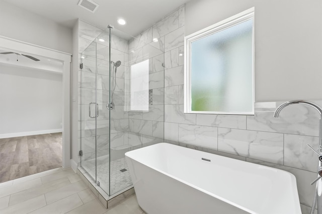 bathroom featuring wood-type flooring, shower with separate bathtub, ceiling fan, and tile walls