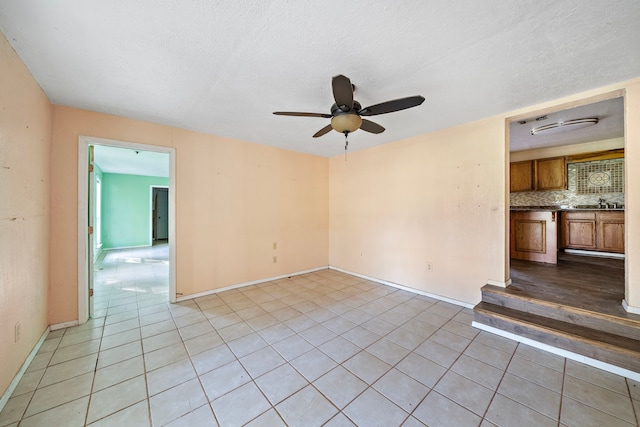 tiled empty room featuring a textured ceiling, ceiling fan, and sink