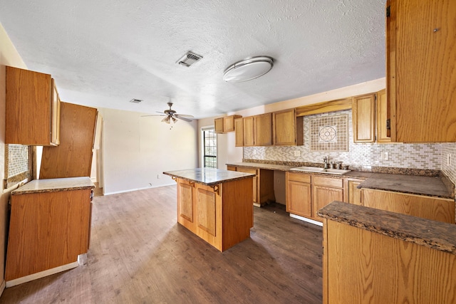 kitchen with sink, ceiling fan, a textured ceiling, a center island, and dark wood-type flooring