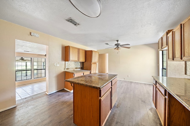 kitchen featuring a textured ceiling, light stone counters, hardwood / wood-style flooring, and a kitchen island