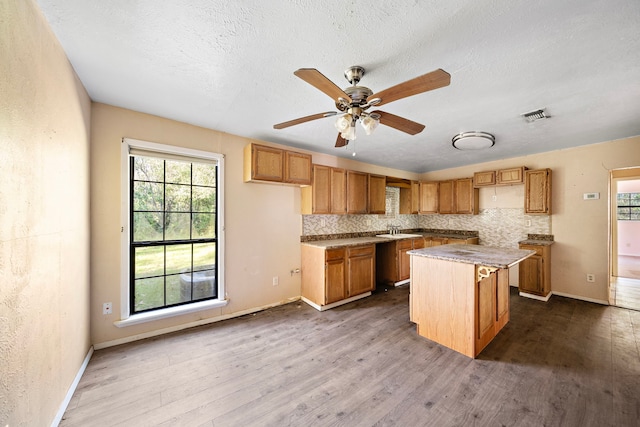 kitchen with a kitchen island, a textured ceiling, sink, decorative backsplash, and hardwood / wood-style flooring