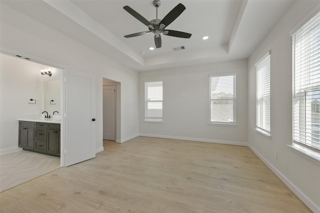 unfurnished room featuring a raised ceiling, a wealth of natural light, light hardwood / wood-style flooring, and ceiling fan